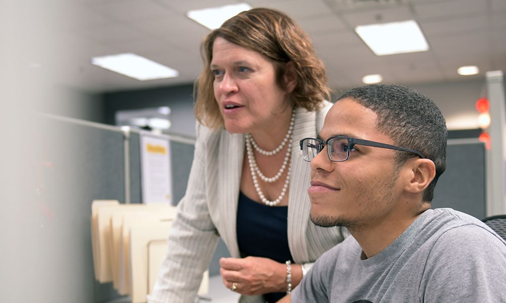 A woman training a man while both look at a screen