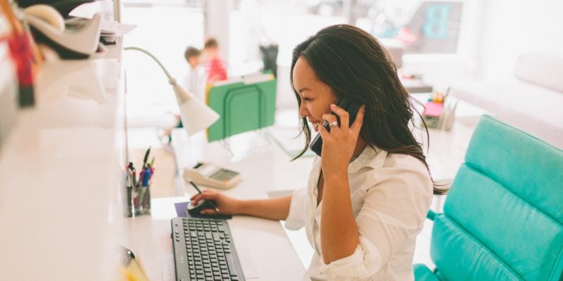 woman sitting at desk with phone to ear looking at computer screen