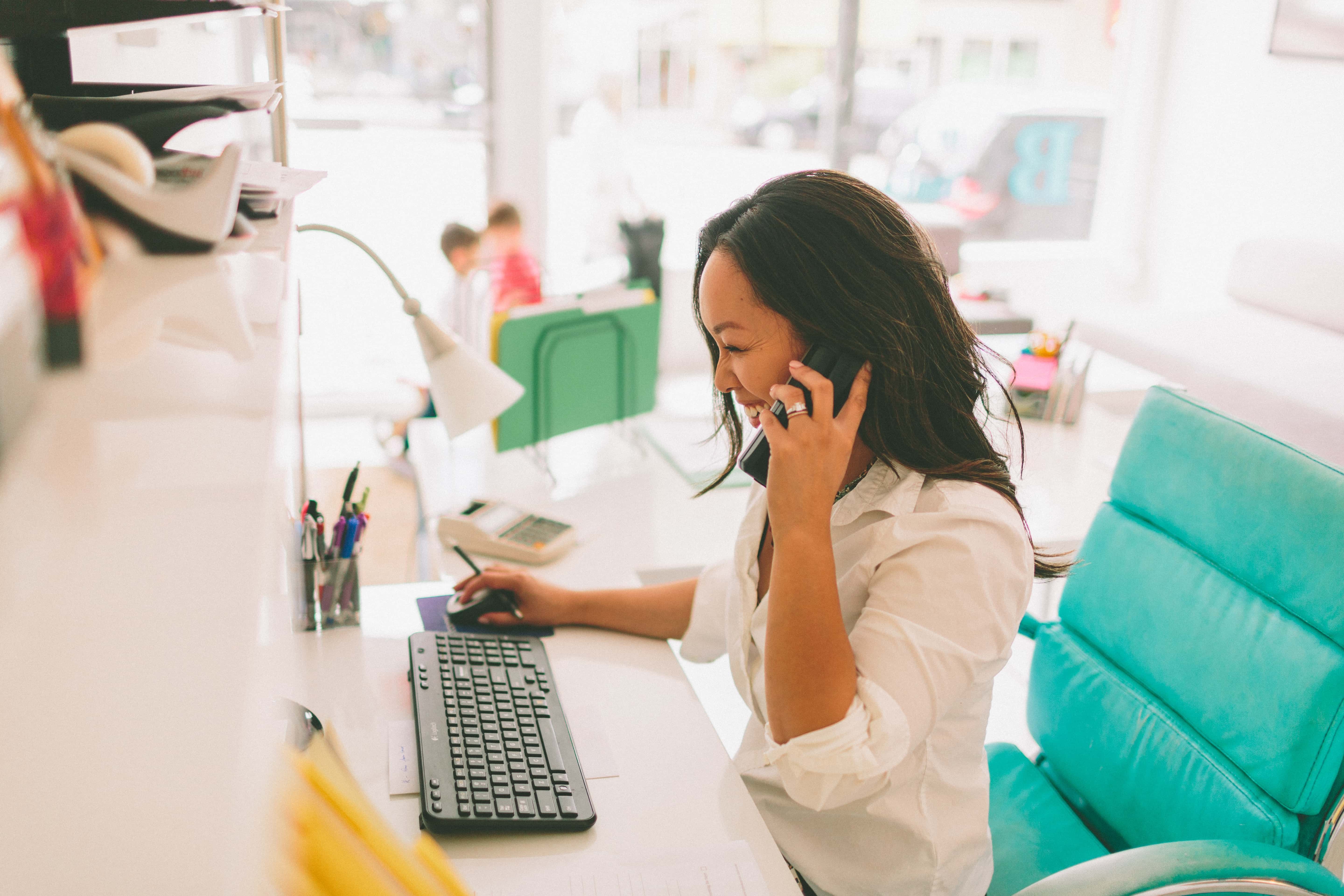 woman sitting at desk with phone to ear looking at computer screen