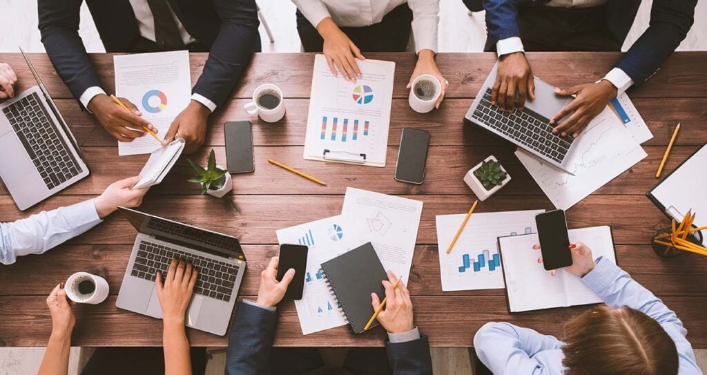 Image of office workers sitting around a table filled with data charts, computers, coffee, and focused on Lead generation trends 2025