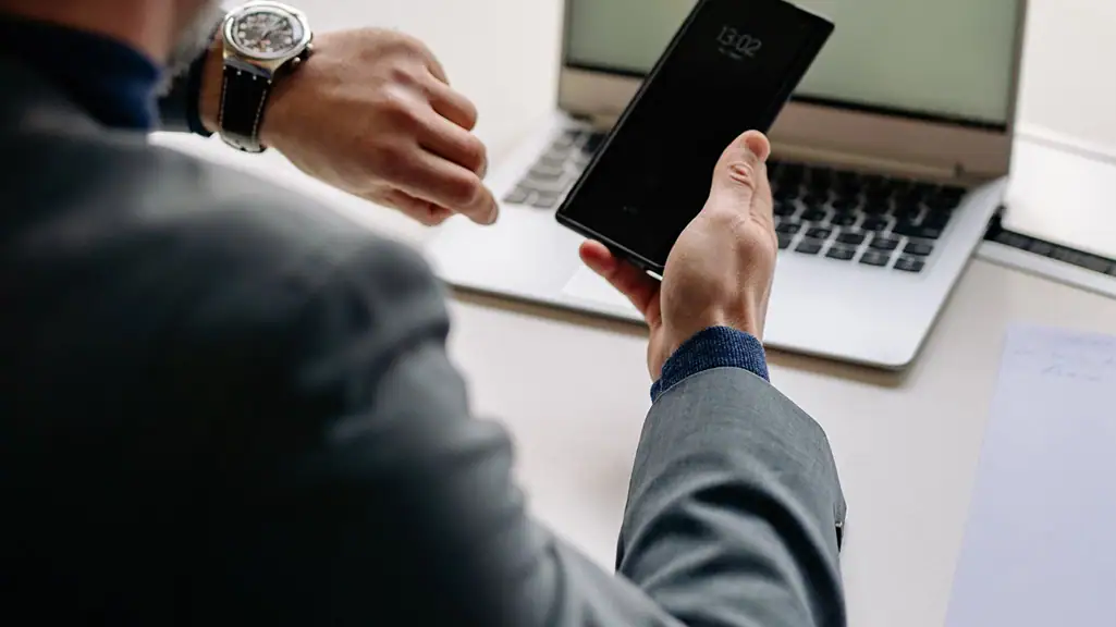 Man on phone checking watch with computer in the background